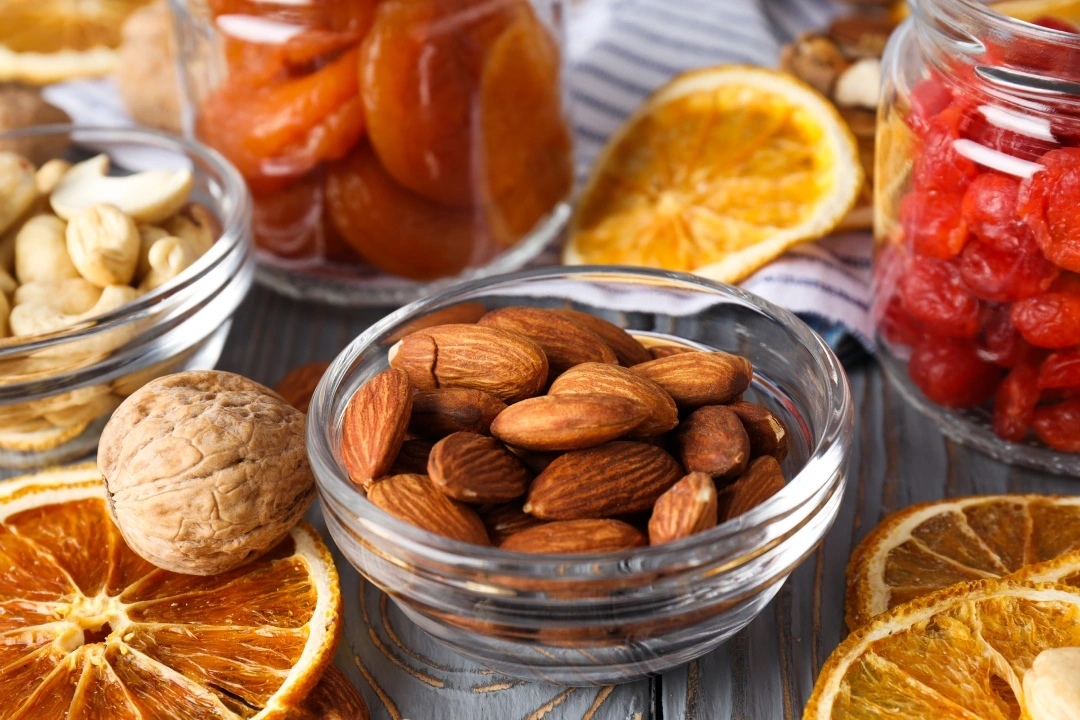 Almonds and dried citrus fruits arranged in glass bowls on wooden surface.