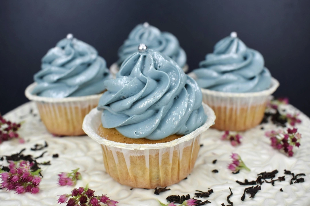 Four vanilla cupcakes with blue frosting swirls arranged on decorative sprinkles.