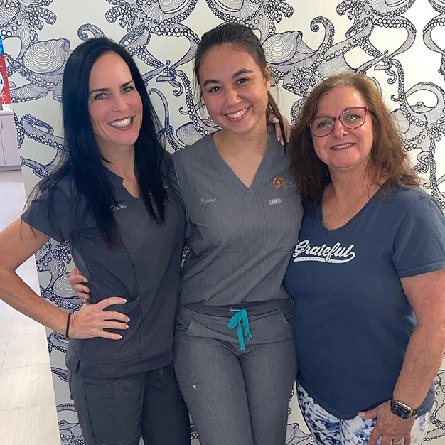 Three women in medical scrubs smiling together at Statler Orthodontics office.