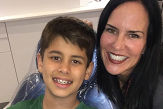 Woman and young boy smiling together indoors, orthodontics office setting.