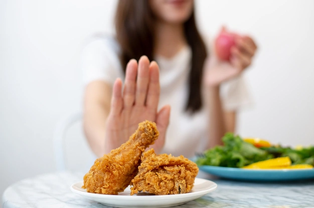 Woman rejecting fried chicken with hand gesture, healthy food choice concept.