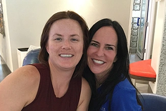 Two smiling women posing together in a bright orthodontic office setting.