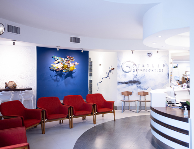 Modern orthodontic office waiting area with red chairs, blue accent wall, and reception desk.