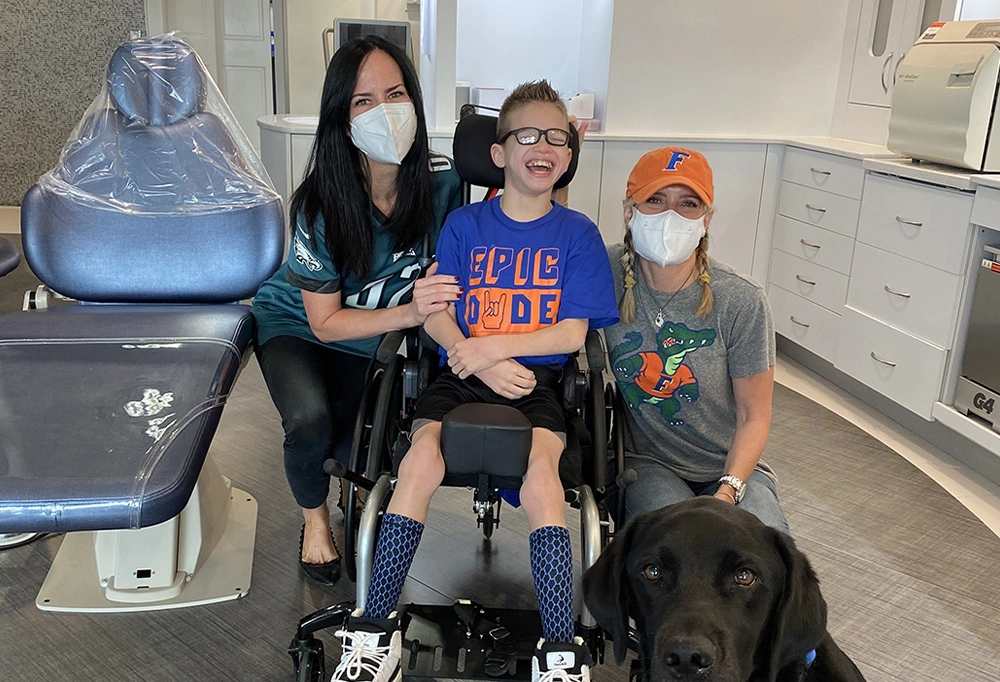 Four people and a dog pose together in an orthodontic office near medical equipment.