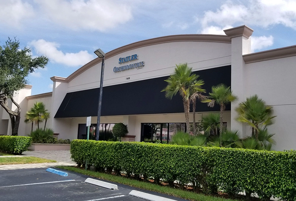 Modern orthodontic office building with curved roof, palm trees, and professional landscaping under blue sky.
