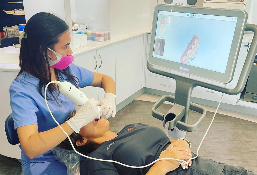 Orthodontist examines dental model on monitor while holding demonstration teeth model in clinical setting.