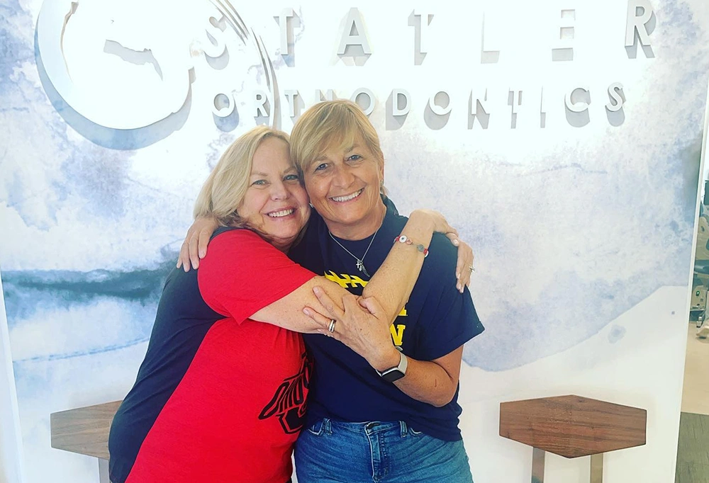 Two women smiling and hugging in front of Statler Orthodontics office signage.
