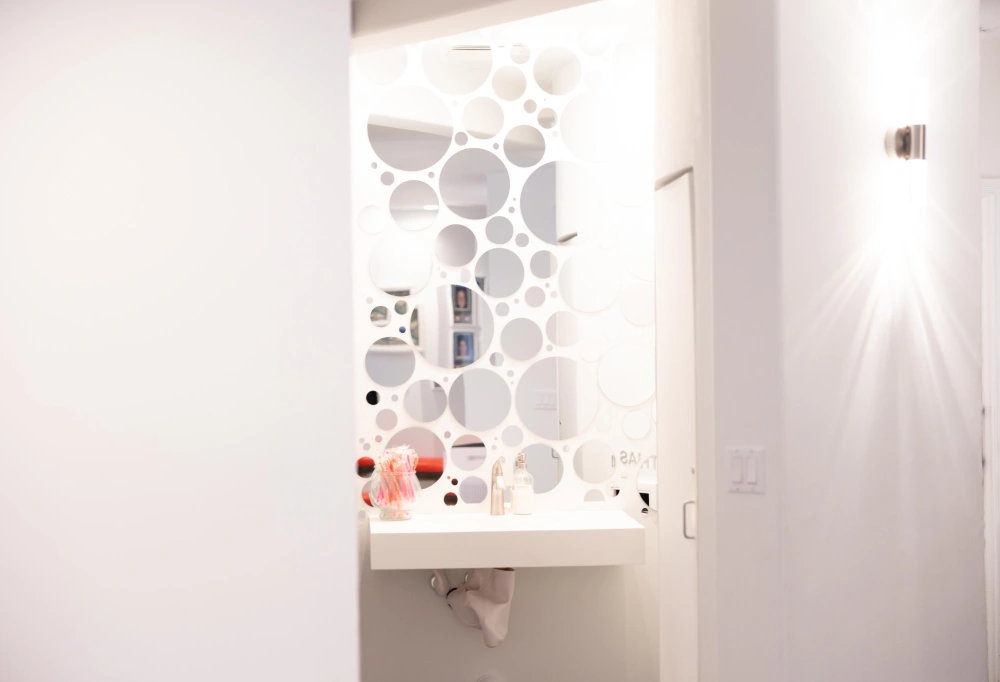 Modern bathroom sink with decorative circular tile pattern and mounted mirror in bright clinical setting.
