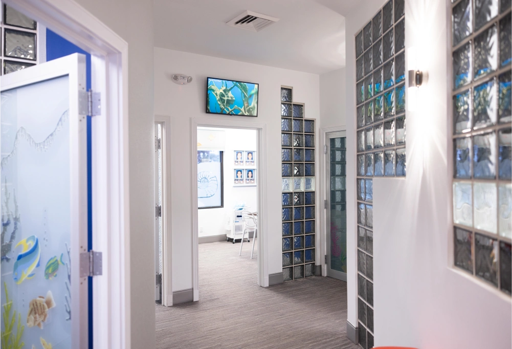 Modern orthodontic office hallway with treatment rooms, storage cabinets, and clinical displays.
