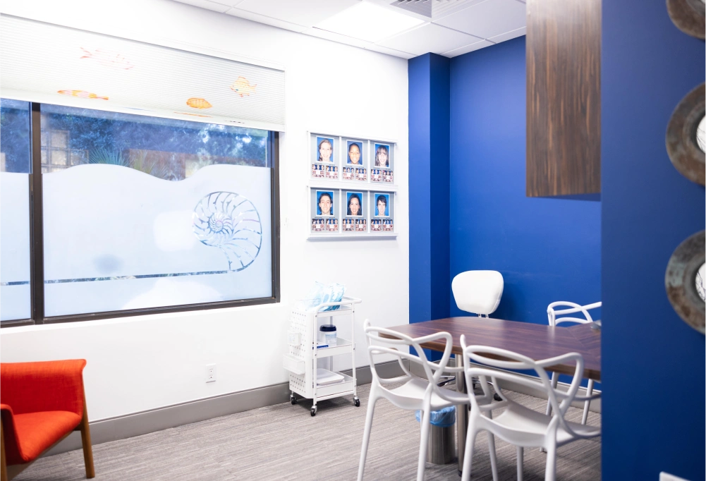 Modern orthodontic consultation room with blue walls, whiteboard, and patient seating area.