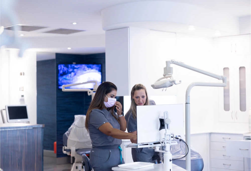 Orthodontist and assistant examining patient in modern dental treatment room with digital display.