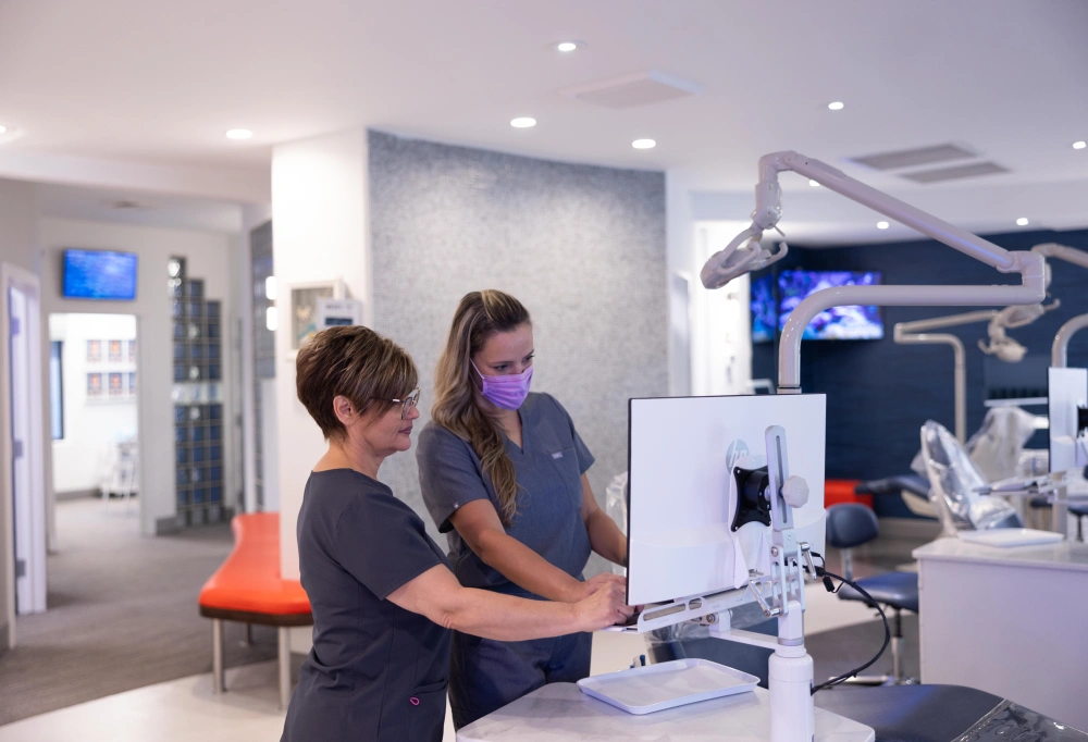 Two dental professionals examine patient records at reception desk in modern orthodontic clinic.