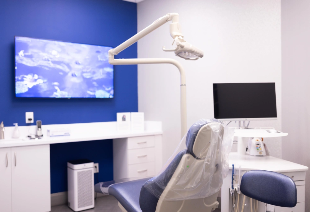 Modern orthodontic treatment room with dental chair, monitor displays, and blue accent wall.