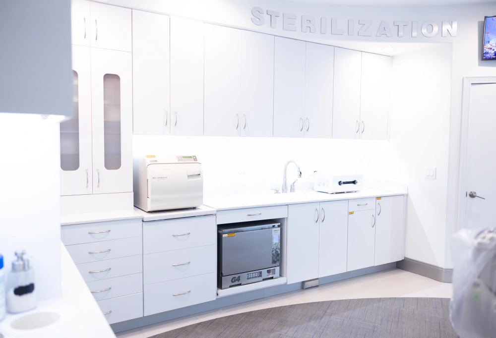 Modern orthodontic office sterilization and lab equipment area with white cabinetry and countertops.