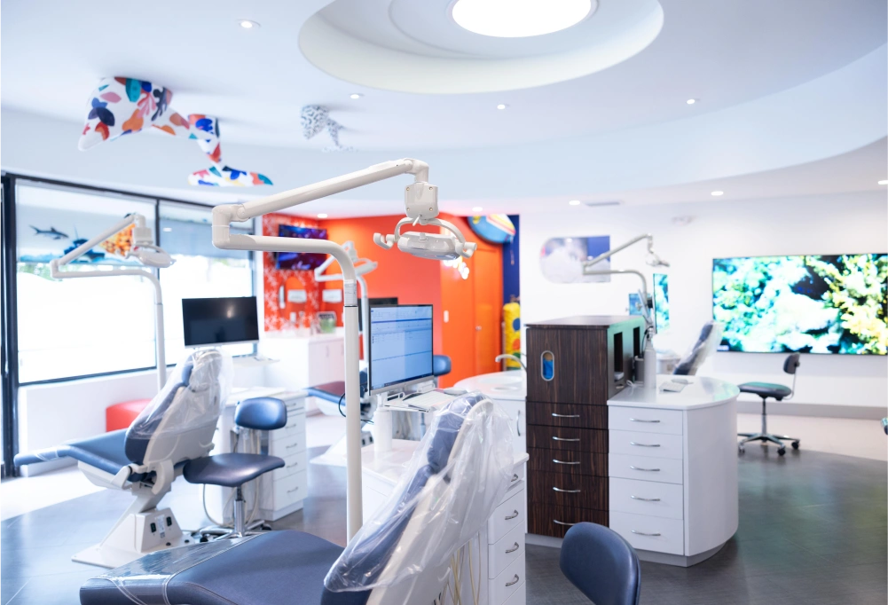 Modern orthodontic treatment room with dental chair, equipment, and bright orange accent wall at Statler Orthodontics clinic.