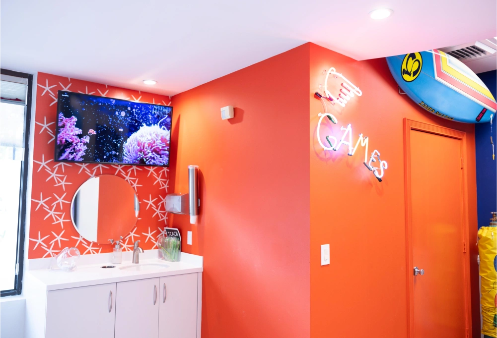 Bright orange orthodontic office room with aquarium, refrigerator, and colorful wall decorations.