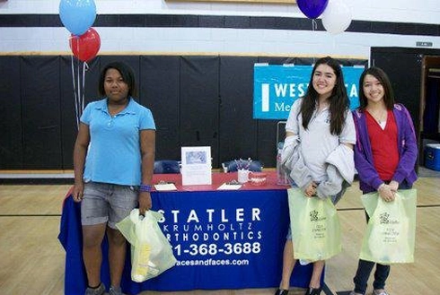 Statler Orthodontics team members at promotional booth with balloons and branded materials in gymnasium.