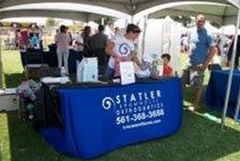Statler Orthodontics booth at outdoor community event with staff and visitors under tent.