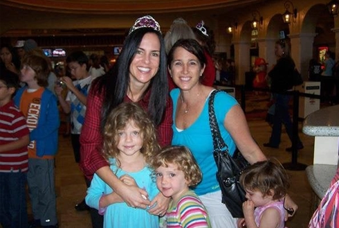 Two women and two children smiling at indoor event or gathering.