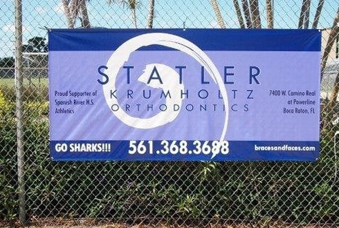 Blue orthodontics sign on chain-link fence advertising Statler Orthodontics with phone number and website.