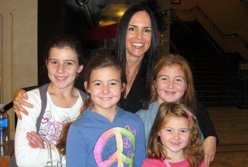 Woman with four children smiling together indoors at what appears to be a social gathering or event.