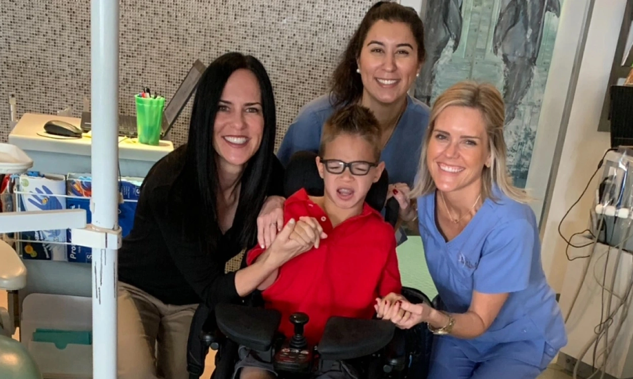 Four people smiling together in an orthodontic office setting with dental equipment visible.