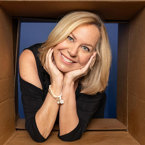 Professional woman smiling at camera in black top against blue background, hands posed near face.