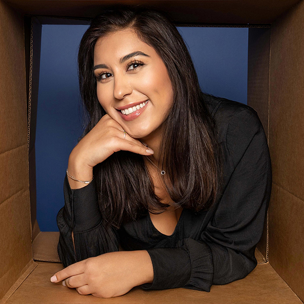 Professional woman in black blazer smiling at camera against blue background, orthodontics office setting.