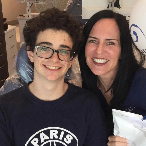 A teenage boy and adult woman smile together indoors at an orthodontics office.