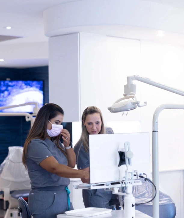 Two dental professionals in masks examine patient records in a modern orthodontic office treatment room.