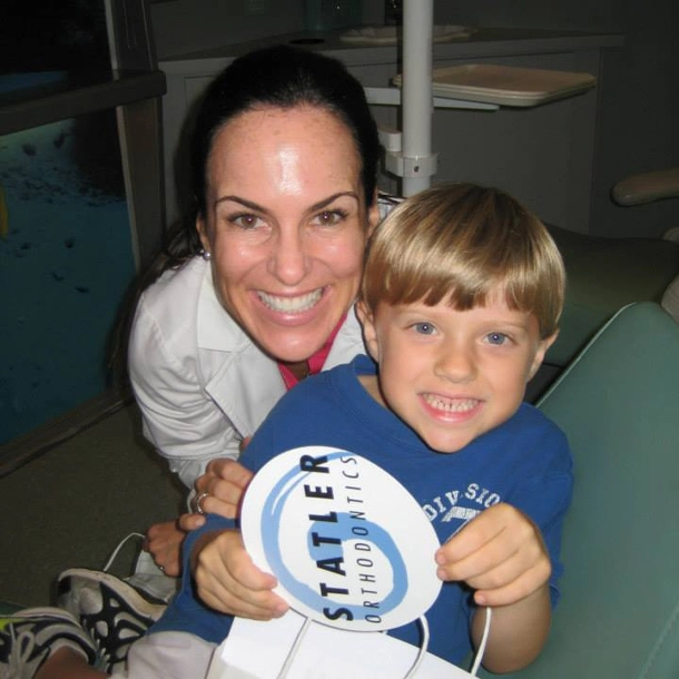 Woman and young boy holding Statler Orthodontics branded item in office setting.