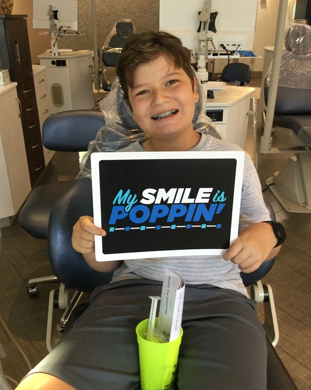 Young patient in dental chair holding "My Smile is Winning" tablet at orthodontics office.
