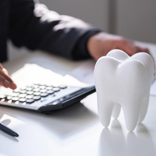White tooth model on desk beside calculator, orthodontist working in background