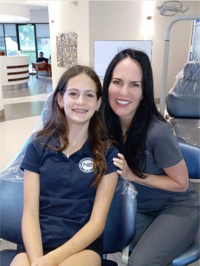 Two women in navy Statler Orthodontics polo shirts smiling together in a modern dental office.