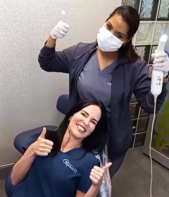 Two dental professionals wearing masks giving thumbs up in an orthodontic office setting.