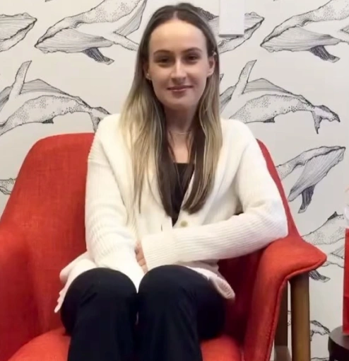 Young woman sitting on red chair wearing white cardigan, smiling at camera in orthodontics office.