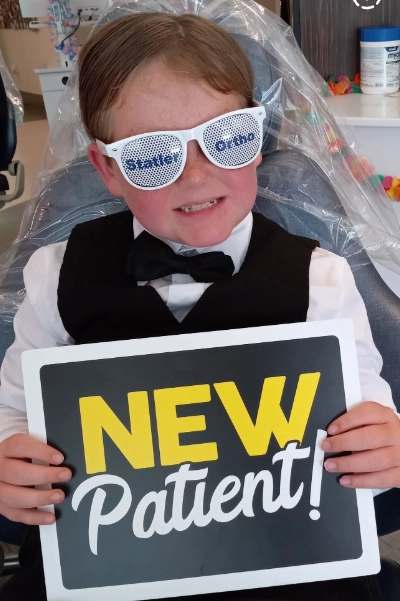Child in orthodontist costume holding "NEW Patient" sign at Statler Orthodontics office.