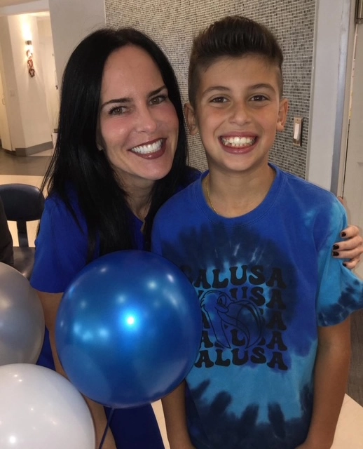 Two people in blue shirts holding a blue bowling ball indoors, smiling at camera.