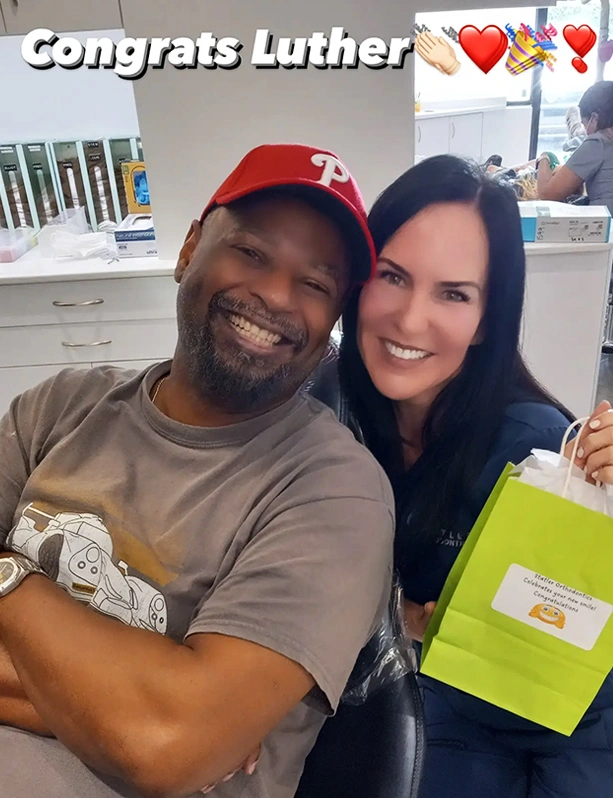 Two people smiling at orthodontic office with "Congrats Luther" text and heart decorations above.