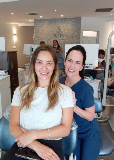 Two women smiling at camera in modern orthodontic office reception area.