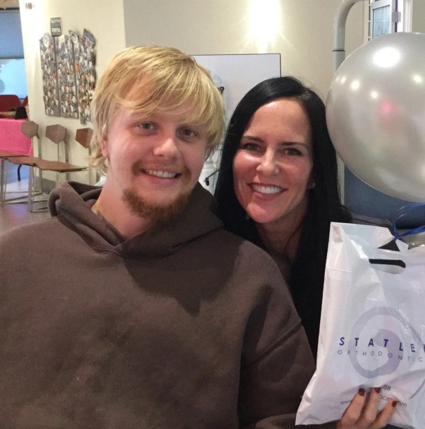 Two people smiling at orthodontics office, holding branded materials indoors.