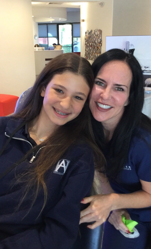 Two smiling women posing together in a bright indoor office setting at Statler Orthodontics.